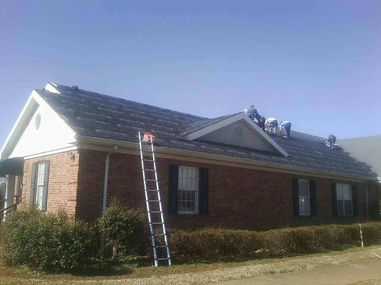 Crew tearing shingles off a brick ranch roof with a ladder set — Emergency Roof Repair work by our crew in Alpharetta