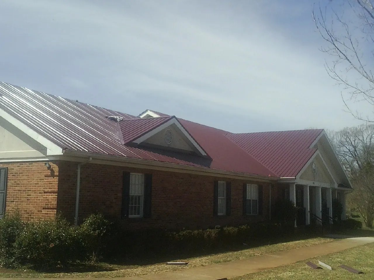 Red metal roof with gabled entries on a long brick building, from a Hail Damage Roof Repair job in Alpharetta