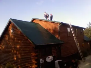 Crew on the ridge of a green metal roof on a two story log home in Alpharetta