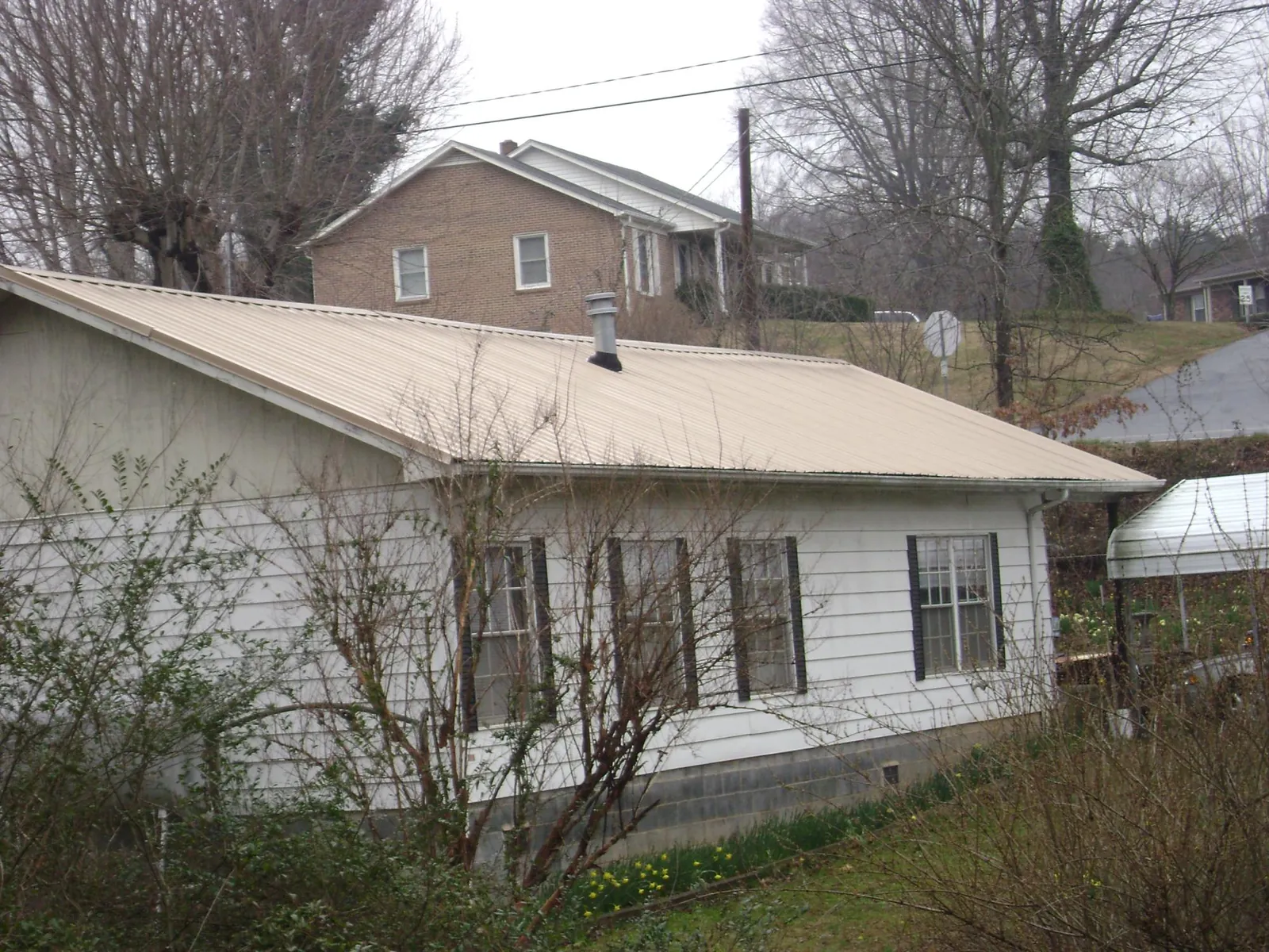 Tan metal roof on a white sided house set into a hillside — Commercial Roofing by Roofing Brothers in Alpharetta